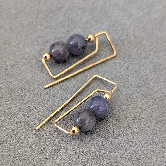 Pair of gold earrings with purple beads on a gray surface