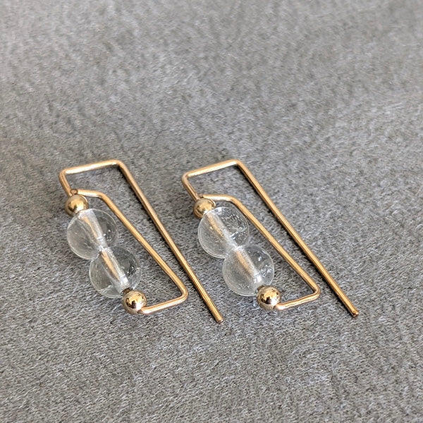 Gold hoop earrings with clear glass beads on a gray surface