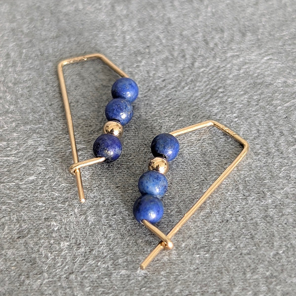 Gold-framed earrings with blue beads on a gray surface