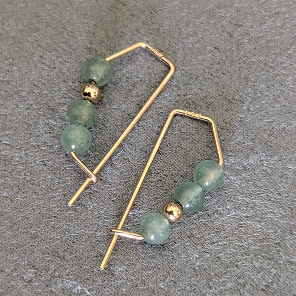 Gold hoop earrings with green beads on a gray surface