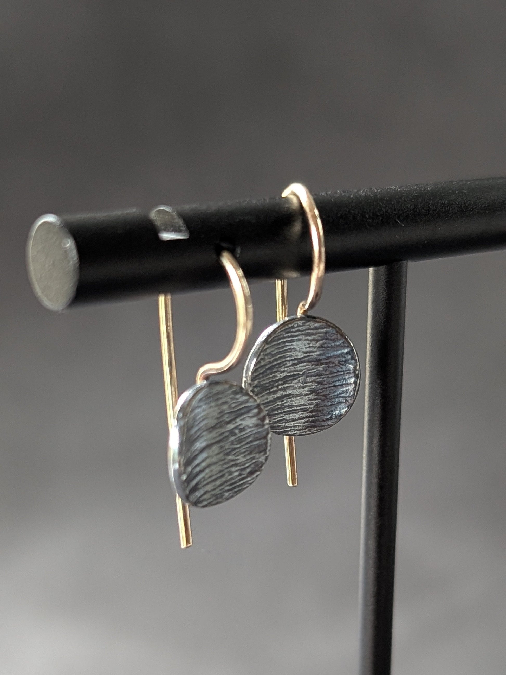 dainty textured charcoal silver disk earrings with 14k gold ear hooks on earring stand