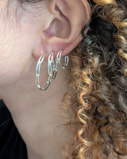 A close-up of a person's ear wearing a cluster of three polished silver hoop earrings.