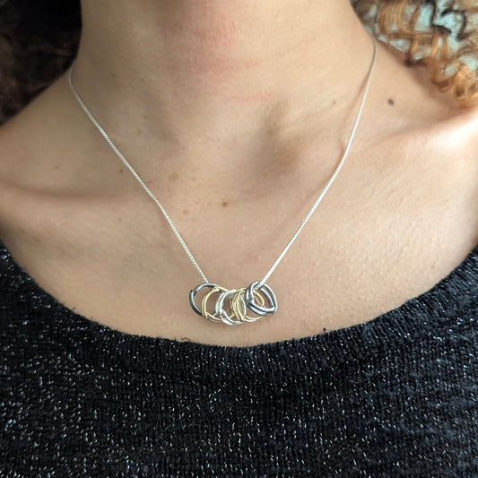 A close-up of a person wearing a delicate silver necklace with five spacer ring charms, paired with a black textured top.