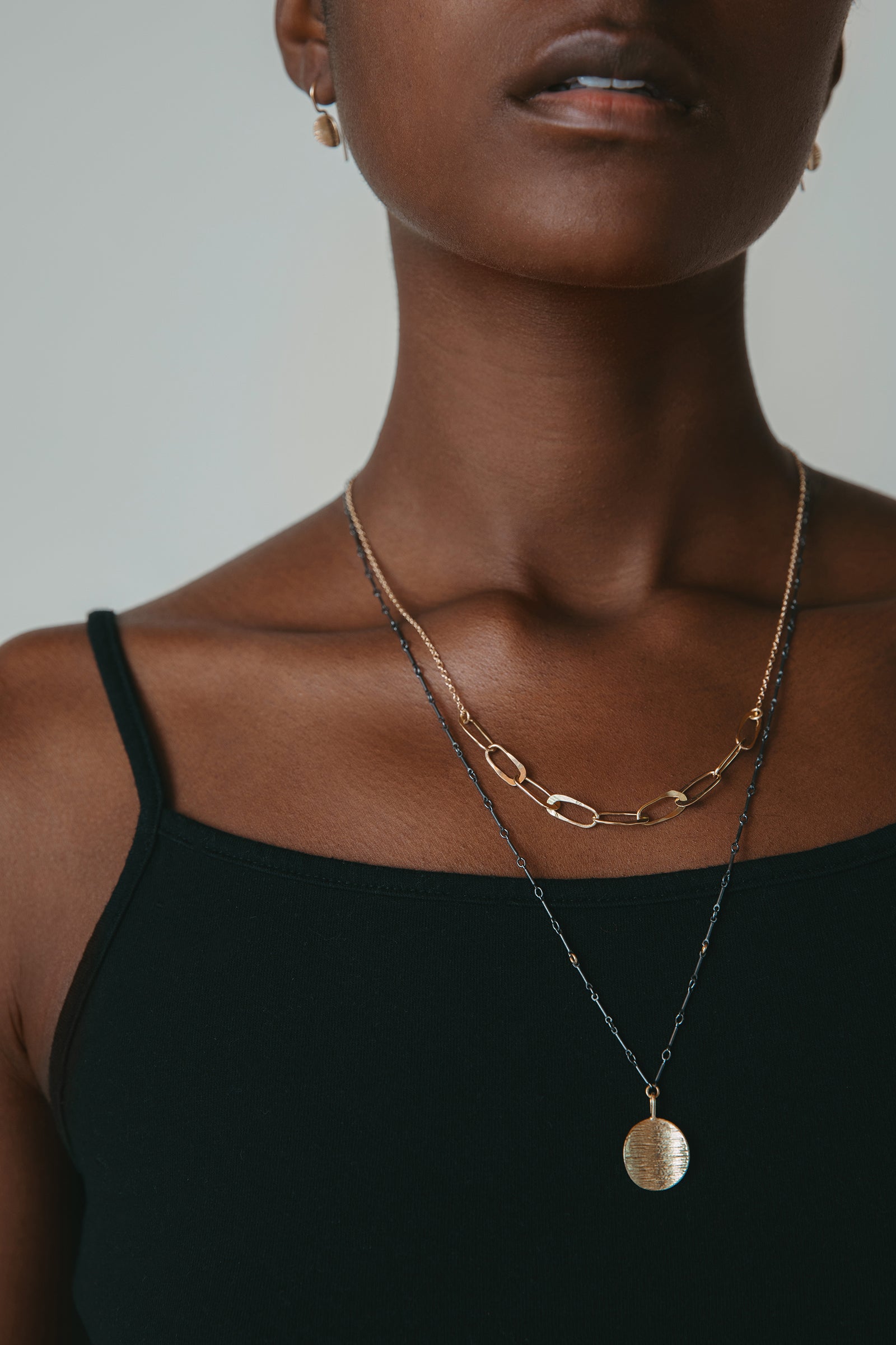 Gold oval chain link necklace and gold circle pendant necklace worn on model