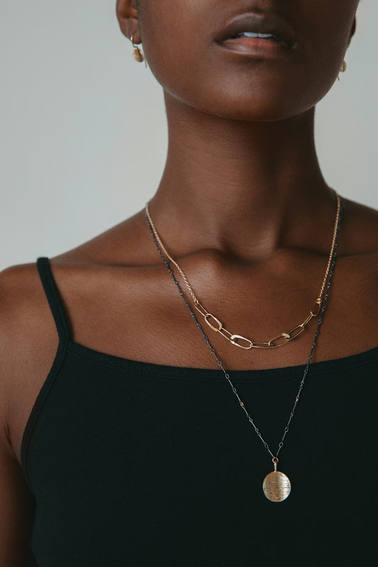 Gold oval chain link necklace and gold circle pendant necklace worn on model