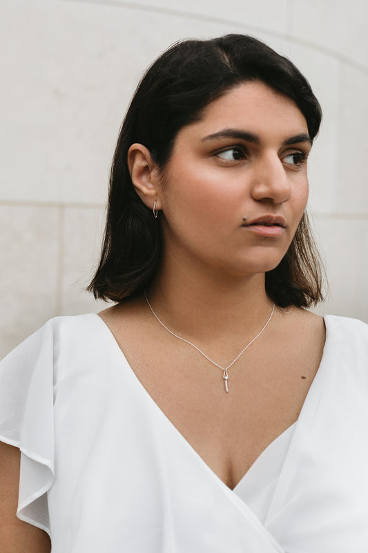 model wearing mini V-shaped charm hoop earrings and a diamond necklace