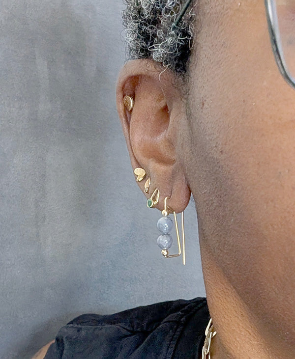 Close-up of an ear wearing multiple gold earrings against a neutral background
