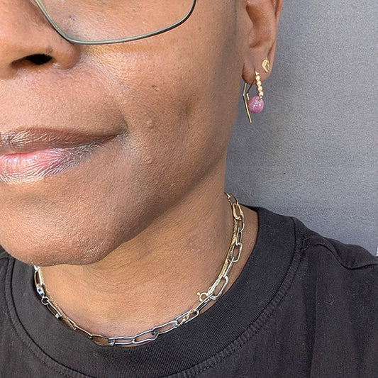 Close-up of a person wearing a gold chain necklace and pink earrings against a gray background