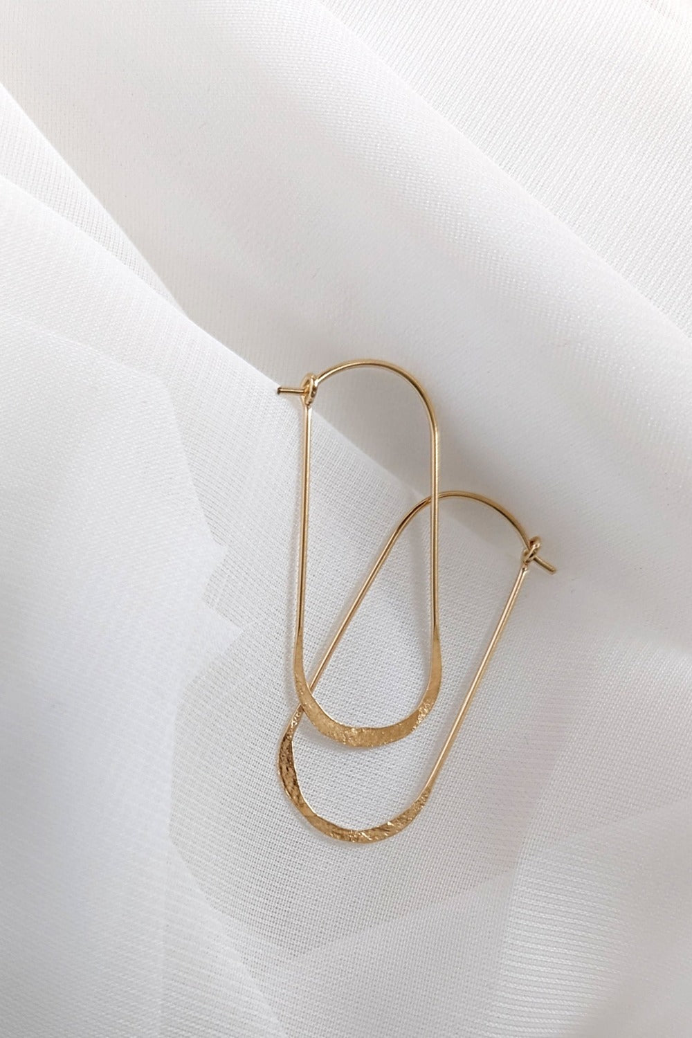 Oval wire hoop earrings in yellow gold styled on white linen