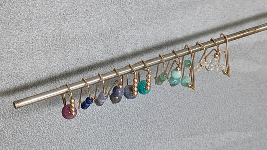 A row of gold hoops with colorful gemstones hanging on steel rod