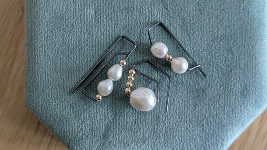Blacken silver hoop earrings accented with white pearls and gold beads on a sage green tray
