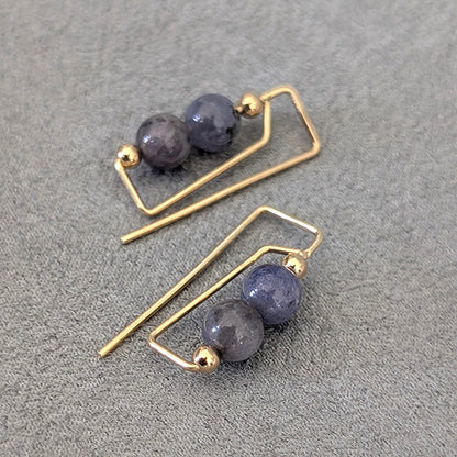 Pair of gold earrings with purple beads on a gray surface