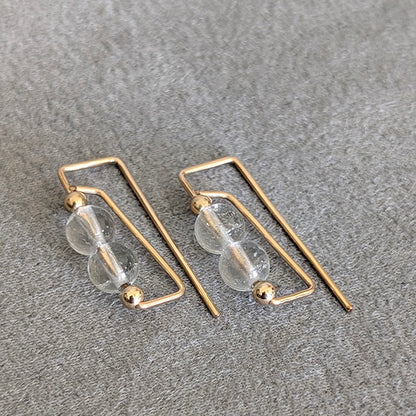 Gold hoop earrings with clear glass beads on a gray surface