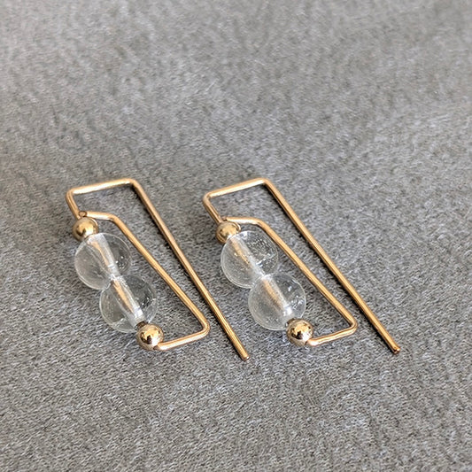 Gold hoop earrings with clear glass beads on a gray surface