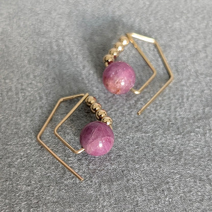 Gold earrings with pink beads on a gray surface