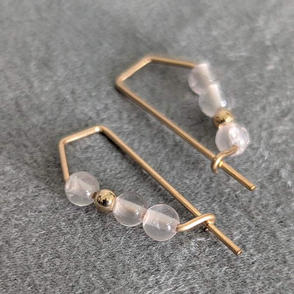Gold earrings with clear beads on a gray surface