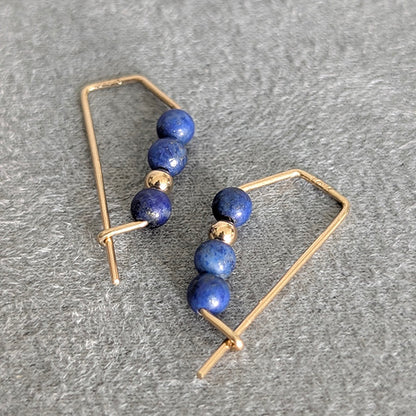 Gold-framed earrings with blue beads on a gray surface