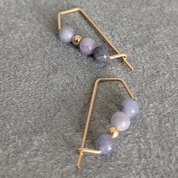 Pair of gold hoop earrings with purple beads on a gray surface