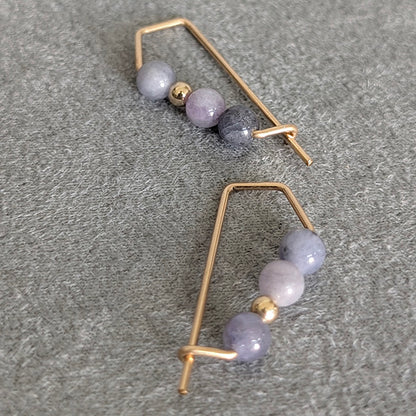 Pair of gold hoop earrings with purple beads on a gray surface