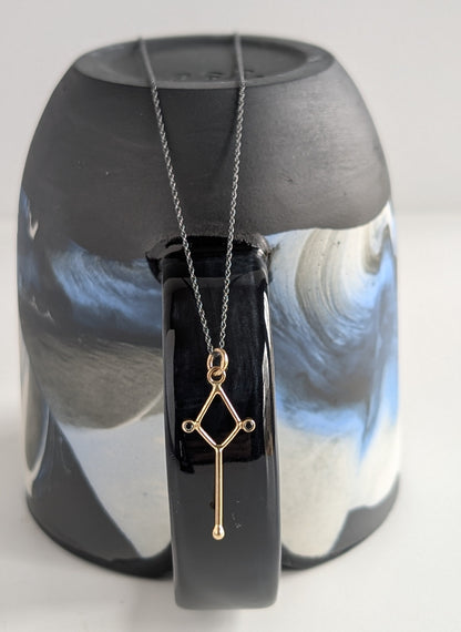 Gold necklace with a geometric pendant on a reflective black surface