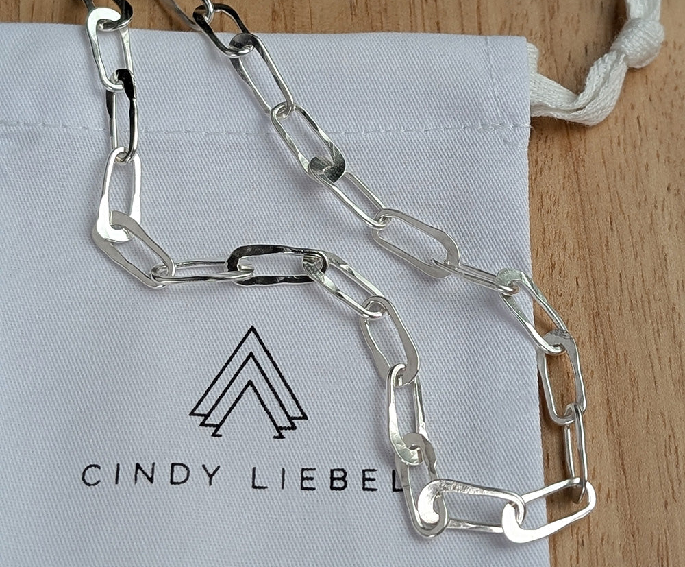 Silver chain necklace on a Cindy Liebel branded pouch with a wooden surface background