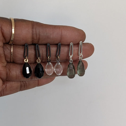 Hand holding five teardrop-shaped earrings on a plain background