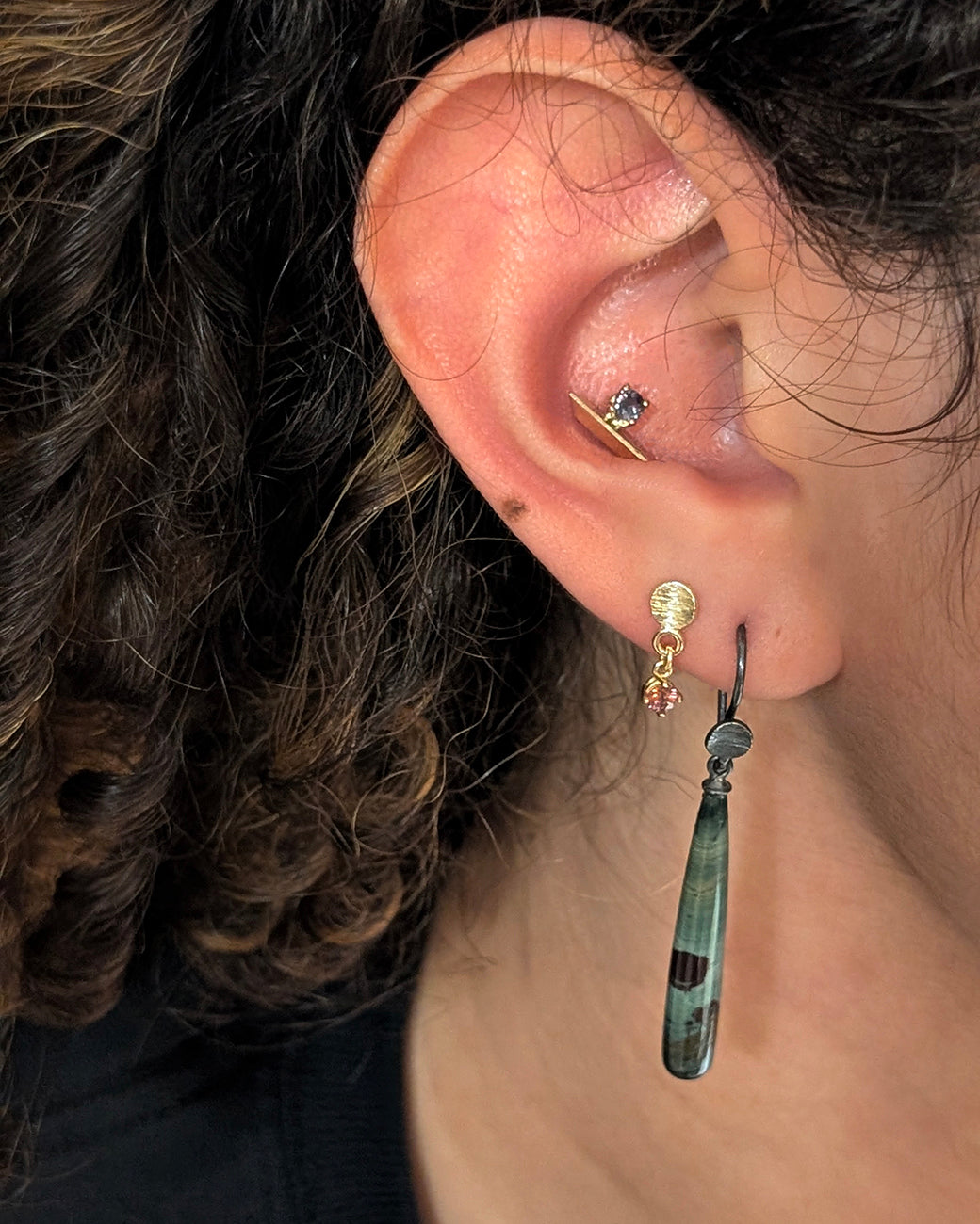 Model wear two pairs of dangle earrings one long one short and gold studs.