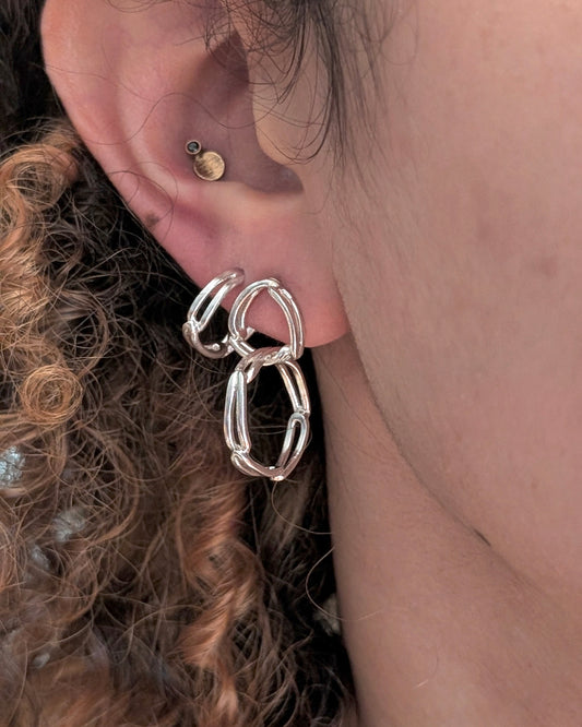 A close-up of a person's ear wearing a silver Huggie hoop earrings and circle post drop link earrings.
