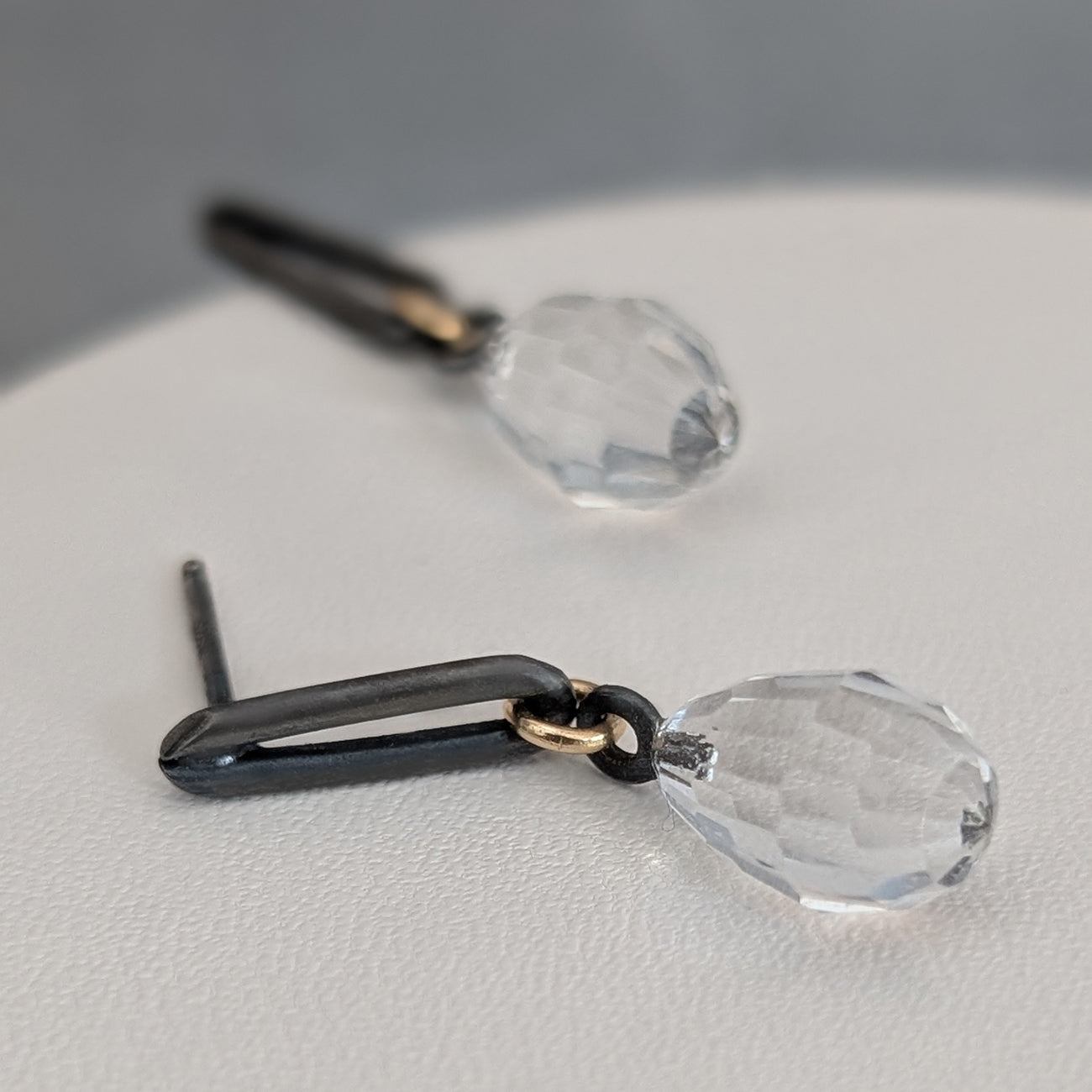 Black and gold earrings with clear teardrop-shaped crystals on a light gray surface.