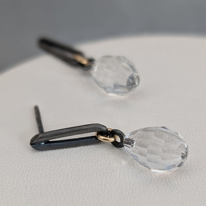 Black and gold earrings with clear teardrop-shaped crystals on a light gray surface.