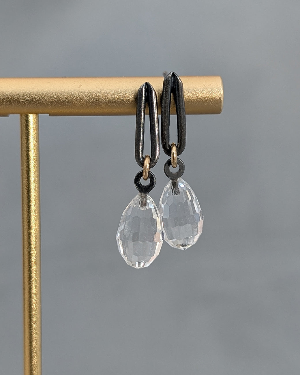 Pair of earrings with clear teardrop-shaped stones on a gold stand against a gray background