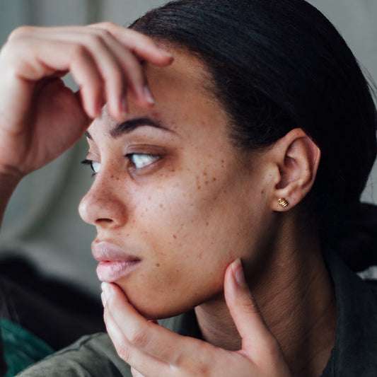 Tiny spiral 14K gold stud earrings worn on model with fabric draped in the background