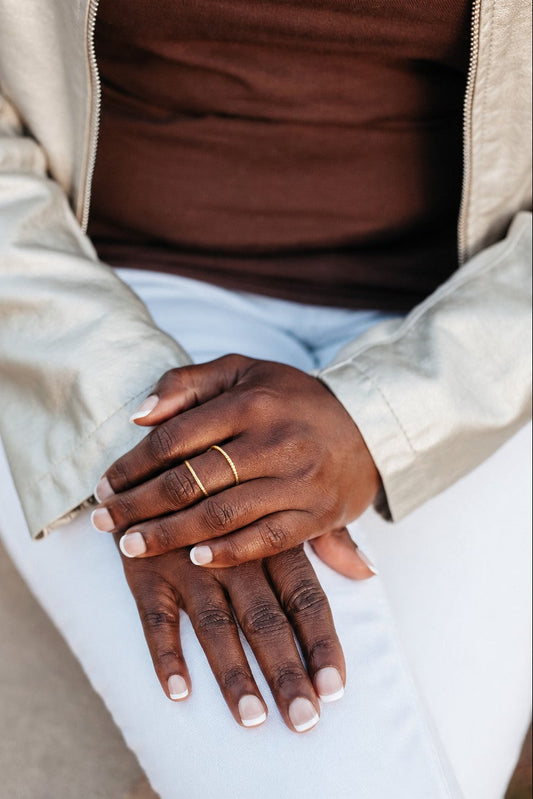 14K gold worn on a person's hand over white pants