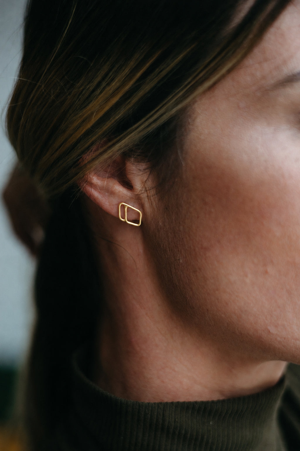 14K gold open diamond shaped, asymmetrical outlined stud earrings styled on model wearing turtleneck 