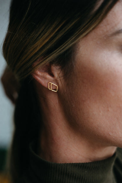 14K gold open diamond shaped, asymmetrical outlined stud earrings styled on model wearing turtleneck 