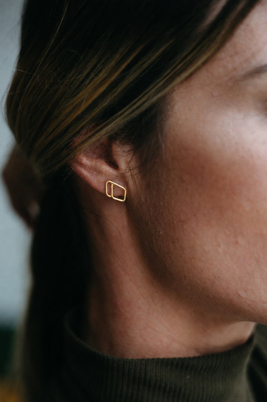 14K gold open diamond shaped, asymmetrical outlined stud earrings styled on model wearing turtleneck 