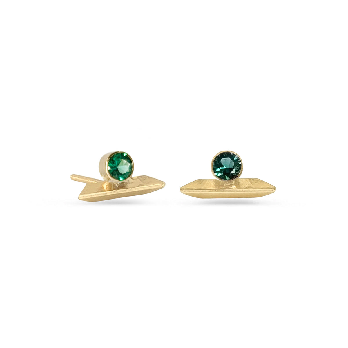 Pair of knife edge stud earrings in gold with round faceted emerald gemstones on white background.