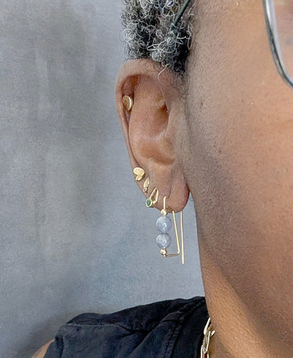 Close-up of an ear wearing multiple gold earrings against a neutral background