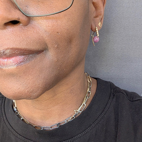 Close-up of a person wearing a gold chain necklace and pink earrings against a gray background