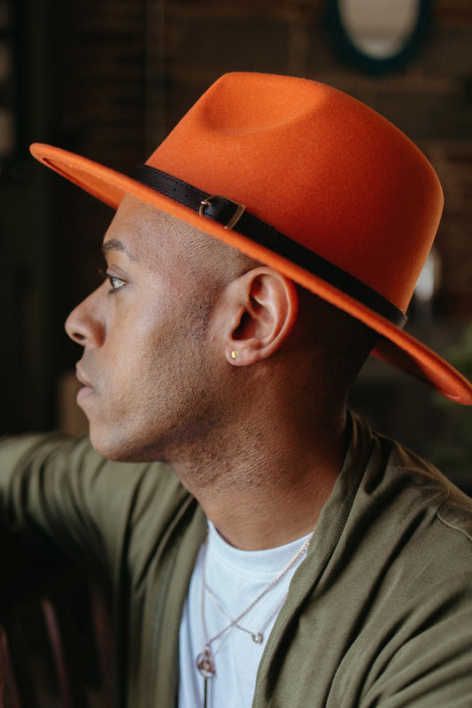 Model wearing tiny gold round disc earrings wearing orange flat bottom hat and green cardigan