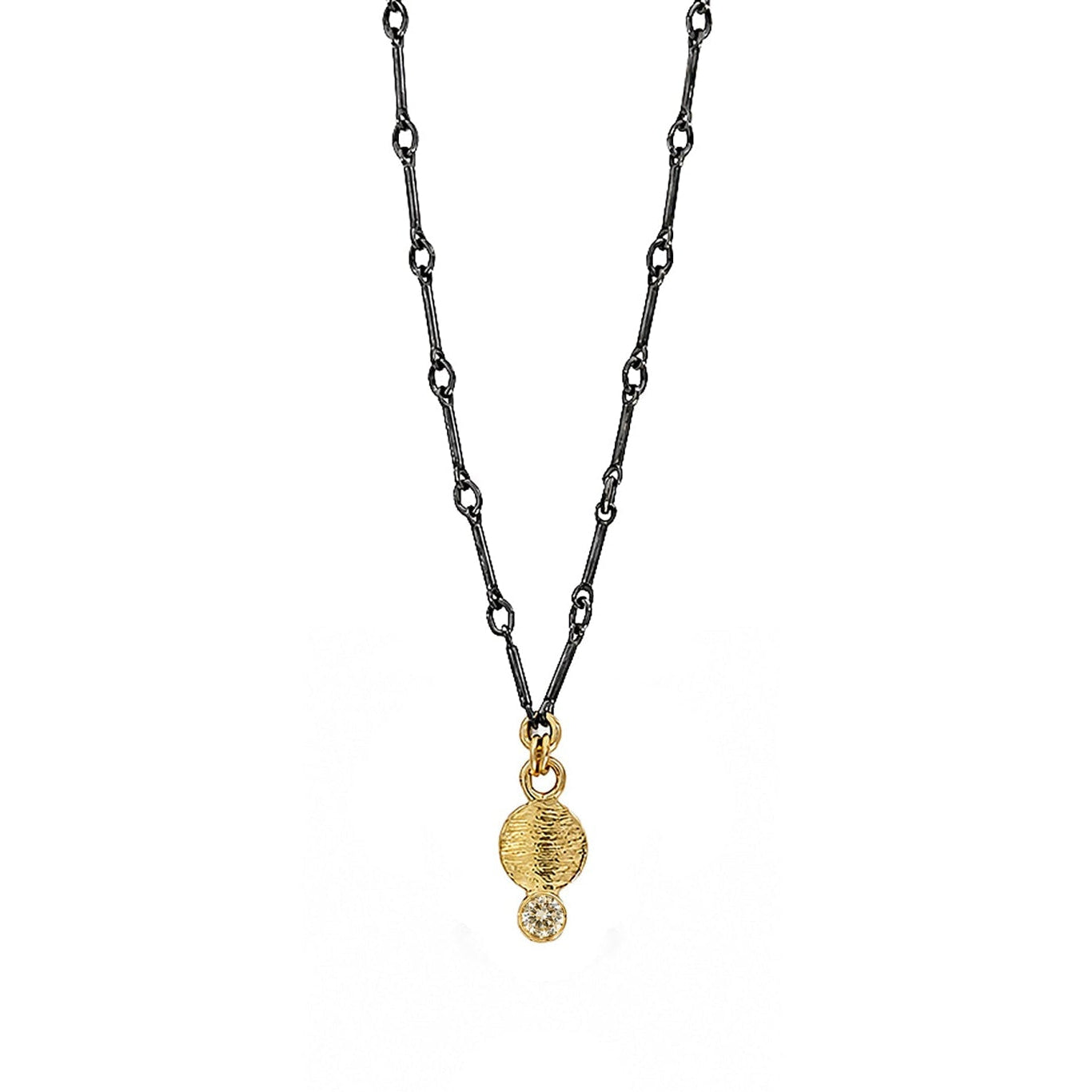 A delicate necklace featuring a dark oxidized chain with a double gold-tone pendant, consisting of a textured disc and a small clear faceted gemstone, shown against a plain white background.