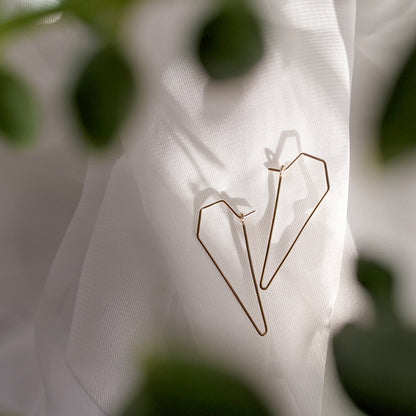 Small dagger wire hoop earrings in gold on white linen