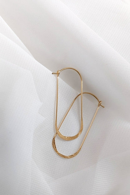 Oval wire hoop earrings in yellow gold styled on white linen
